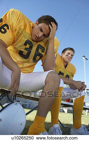 Stock Image - Two football players sitting on bench, low angle view. Fotosearch