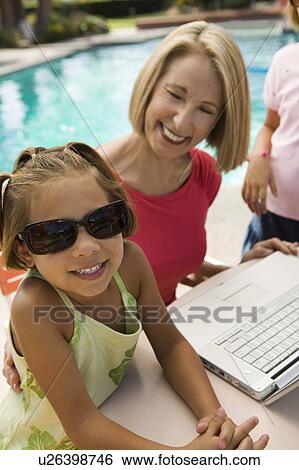 Two girls (7-9) using laptop with grandmother by swimming pool, portrait. View Large Photo Image Stock Photograph - Two girls (7-9) using laptop with grandmother by swimming pool, portrait.. Fotosearch