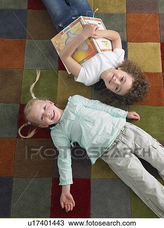 Stock Image - Two girls lying down on library floor, view from above. Fotosearch