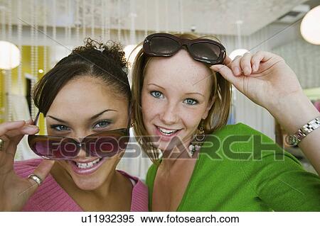 Stock Photography - Two Girls Trying on Sunglasses in Boutique, portrait, close up. Fotosearch