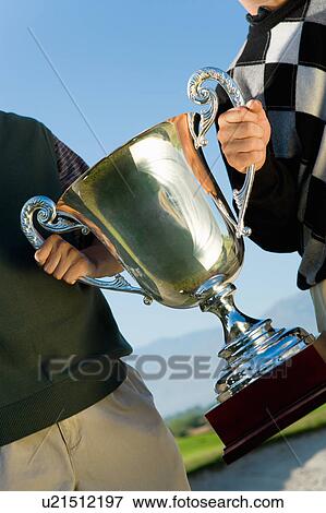 Stock Photo - Two golfers holding trophy together, (portrait), (mid section). Fotosearch