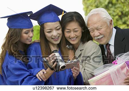 Stock Photo - Two graduates and two guests watching video camera outside. Fotosearch