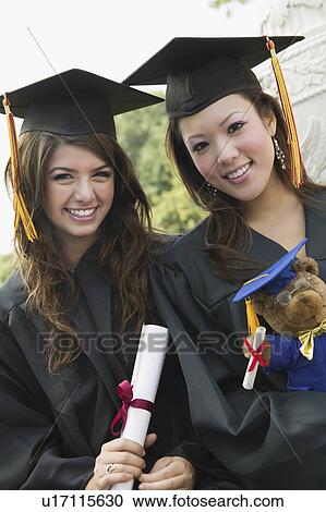 Stock Image - Two graduates holding diploma and teddy bear, portrait. Fotosearch