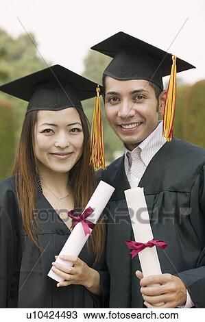 Stock Image - Two graduates holding diplomas outside, portrait. Fotosearch