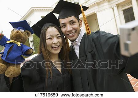 Two graduates taking picture of selves outside View Large Photo Image Stock Photo - Two graduates taking picture of selves outside. Fotosearch