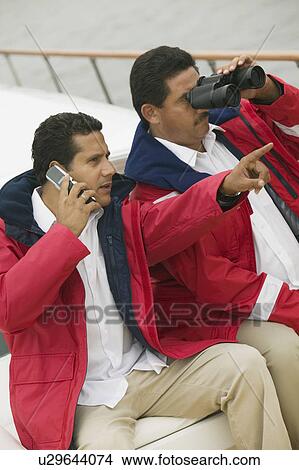 Two men relaxing on yacht, looking through binoculars and talking on mobile phone View Large Photo Image Picture - Two men relaxing on yacht, looking through binoculars and talking on mobile phone. Fotosearch
