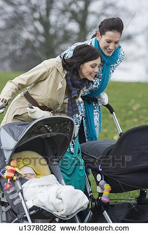 Stock Image - Two mothers in park looking at their babies in strollers. Fotosearch