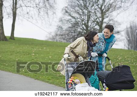 Stock Photo - Two mothers pushing strollers in park. Fotosearch
