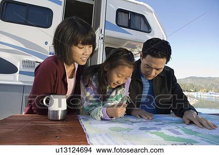 Picture - Two parents and daughter looking at map on picnic table outside RV. Fotosearch
