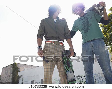 Stock Photo - Two skateboarders laughing, outdoors, low angle view. Fotosearch