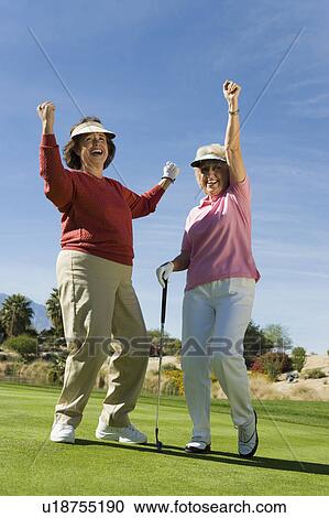 Stock Image - Two women cheering on golf course. Fotosearch