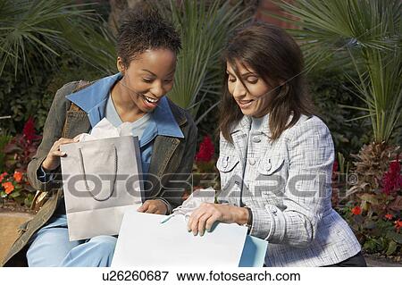 Stock Photo - Two women looking through shopping bags. Fotosearch