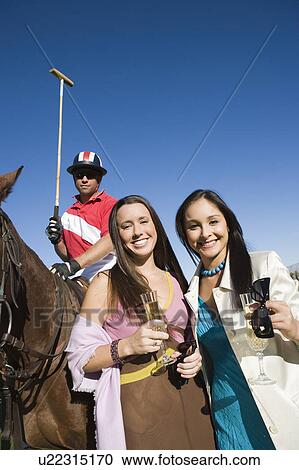 Stock Image - Two women toasting on polo field, portrait. Fotosearch