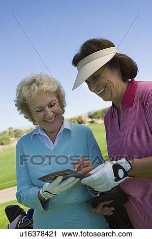 Stock Image - Two women writing in score card on golf course. Fotosearch