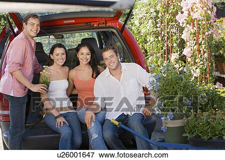 Stock Photo - Two young couples sitting in open car trunk in garden centre, (portrait). Fotosearch