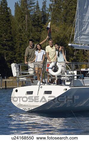 Stock Image - Two young couples standing on stern of sailboat. Fotosearch