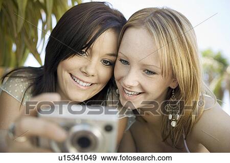 Stock Photo - Two young women looking at pictures on digital camera in backyard, front view. Fotosearch