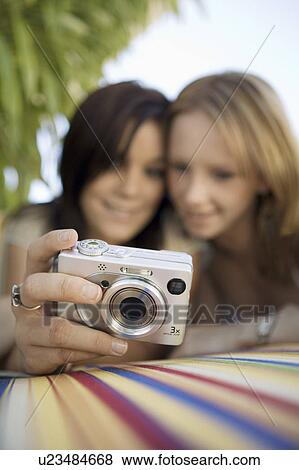 Stock Photo - Two young women looking at pictures on digital camera in backyard, focus on camera, ground view. Fotosearch
