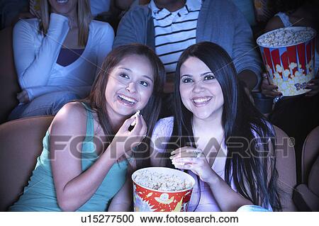 Stock Image - Two young women sharing popcorn in cinema. Fotosearch