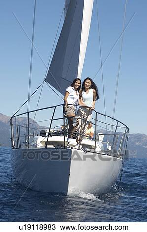 Stock Image - Two young women standing on bow of sailboat. Fotosearch