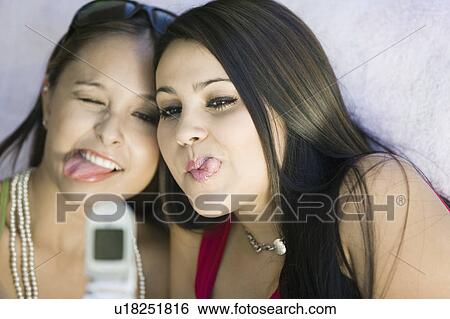 Stock Photograph - Two young women taking funny photo of selves with phone camera, close up. Fotosearch
