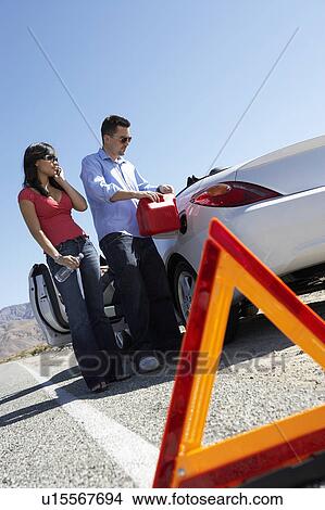 Warning triangle in front of couple pouring fuel into car on desert road View Large Photo Image Picture - Warning triangle in front of couple pouring fuel into car on desert road. Fotosearch