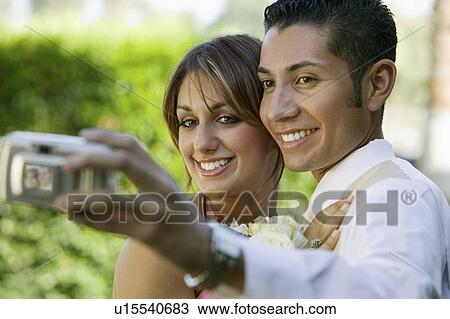 Stock Image - Well-dressed teenage couple taking photograph outside. Fotosearch