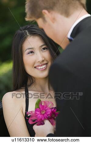 Stock Image - Well-dressed teenage girl receiving corsage from date outside. Fotosearch
