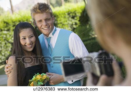 Stock Image - Well-dressed teenager couple posing for video camera outside school dance. Fotosearch