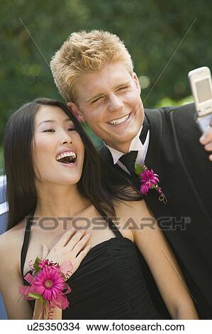 Picture - Well-dressed teenagers taking photo with camera phone outside. Fotosearch