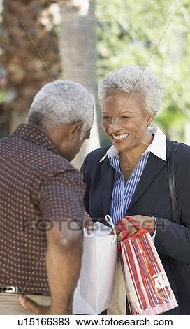 Stock Image - Wife showing husband contents of bag outside. Fotosearch
