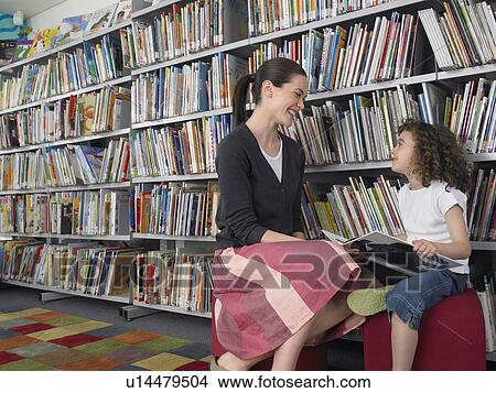 Picture - Woman and girl holding book sitting in library. Fotosearch