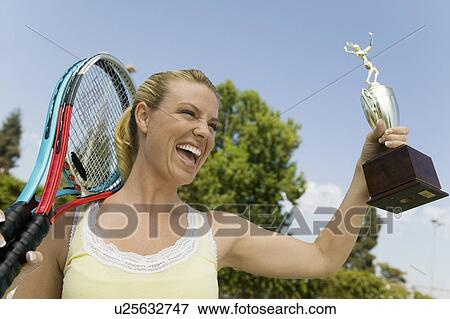 Stock Photo - Woman celebrating on tennis court with Tennis Rackets and Trophy. Fotosearch