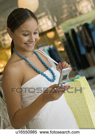 Woman Checking Cell Phone While Shopping in clothing store View Large Photo Image Stock Photography - Woman Checking Cell Phone While Shopping in clothing store. Fotosearch