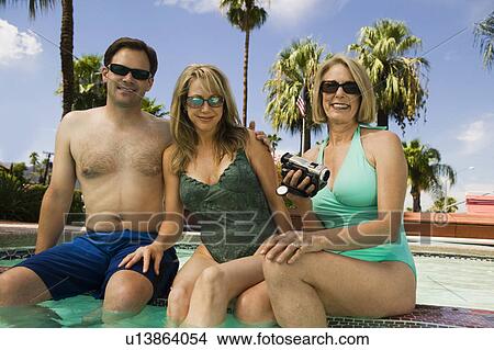 Woman holding camcorder with couple at swimming pool, portrait. View Large Photo Image Picture - Woman holding camcorder with couple at swimming pool, portrait.. Fotosearch
