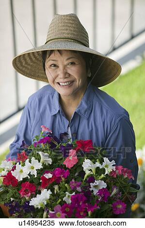 Stock Photography - Woman holding flowers in garden, (portrait). Fotosearch