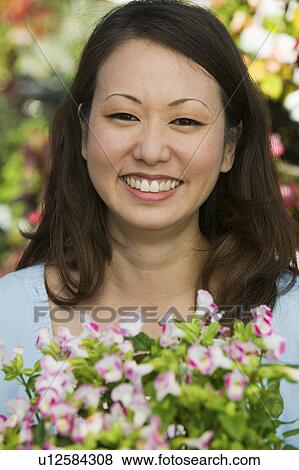 Stock Photo - Woman Holding Flowers in plant nursery, portrait, close up. Fotosearch