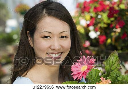 Stock Photograph - Woman Holding Flowers in plant nursery, portrait, close up. Fotosearch