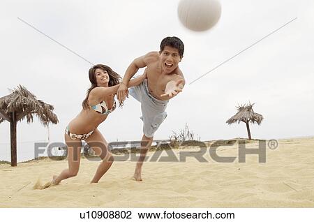 Stock Image - Woman Holding Man Back from Diving for Volleyball on Beach. Fotosearch
