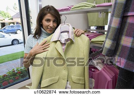 Woman holding up outfit in clothes store, portrait View Large Photo Image Picture - Woman holding up outfit in clothes store, portrait. Fotosearch