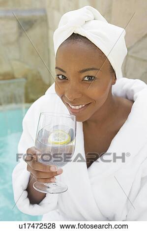 Stock Photo - Woman in bathrobe drinking a glass of water at spa. Fotosearch