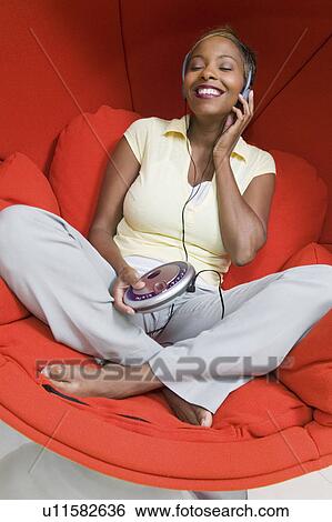 Stock Photograph - Woman in Chair egg chair listening to portable CD player, front view. Fotosearch