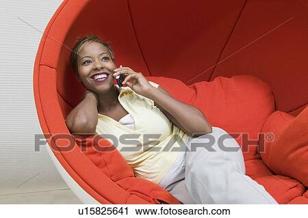 Stock Image - Woman in Chair egg Talking on Cell Phone, front view. Fotosearch