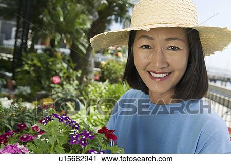 Stock Image - Woman in straw hat gardening, (portrait). Fotosearch