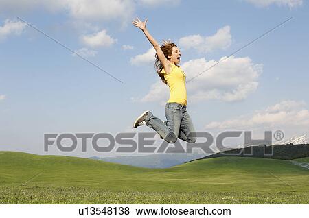Stock Photo - Woman jumping for joy in mountain meadow, side view. Fotosearch
