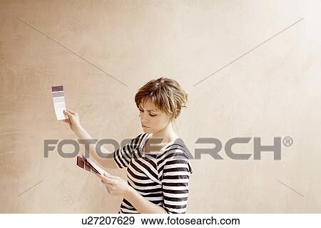 Stock Photo - Woman looking at paint colour swatches in unrenovated room. Fotosearch