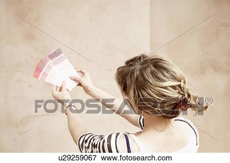 Stock Photo - Woman looking at paint colour swatches in unrenovated room, back view. Fotosearch