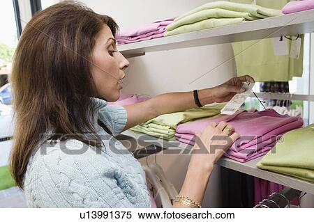 Woman looking at price tag on clothing, side view View Large Photo Image Stock Photography - Woman looking at price tag on clothing, side view. Fotosearch
