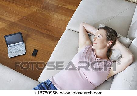 Stock Photograph - Woman lying down on couch, laptop in background, view from above.. Fotosearch