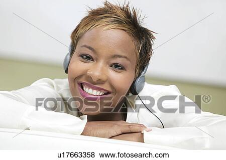 Stock Photo - Woman on couch Listening to Headphones, portrait, close up. Fotosearch